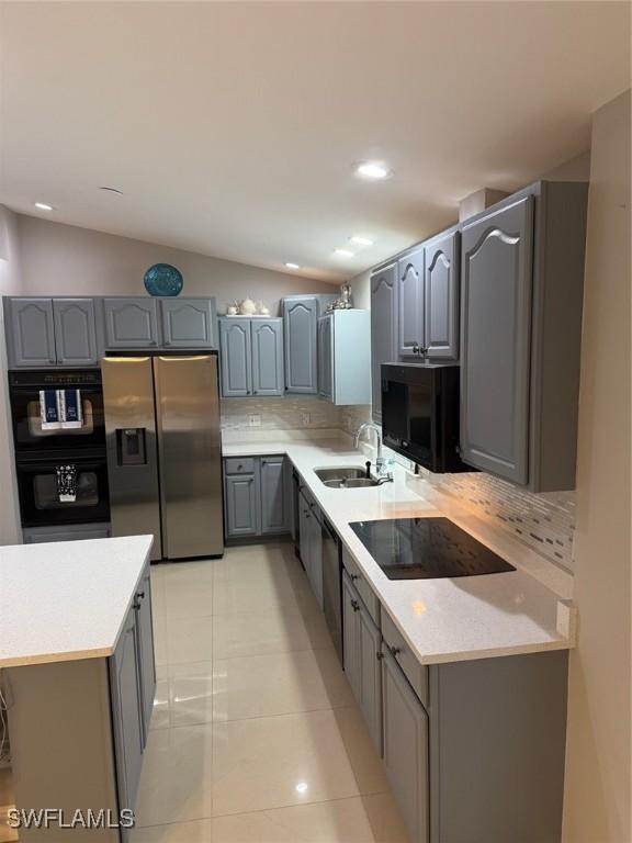 kitchen with gray cabinets, black appliances, lofted ceiling, and a sink
