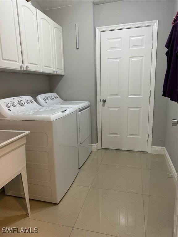 clothes washing area featuring light tile patterned floors, cabinet space, washing machine and dryer, and baseboards