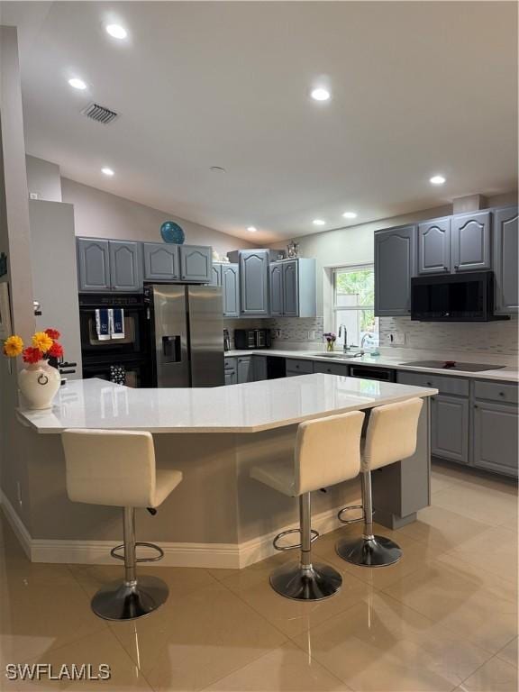 kitchen with a sink, a breakfast bar area, gray cabinetry, visible vents, and black appliances