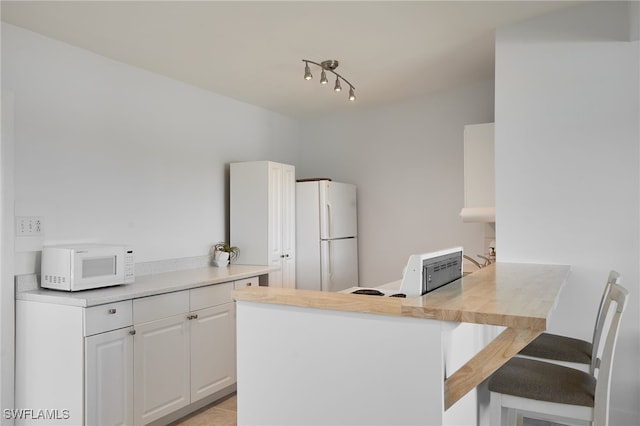 125 Palmetto Cir NE, Port Charlotte, FL 33952 - kitchen featuring white appliances, a kitchen breakfast bar, a peninsula, white cabinets, and light countertops