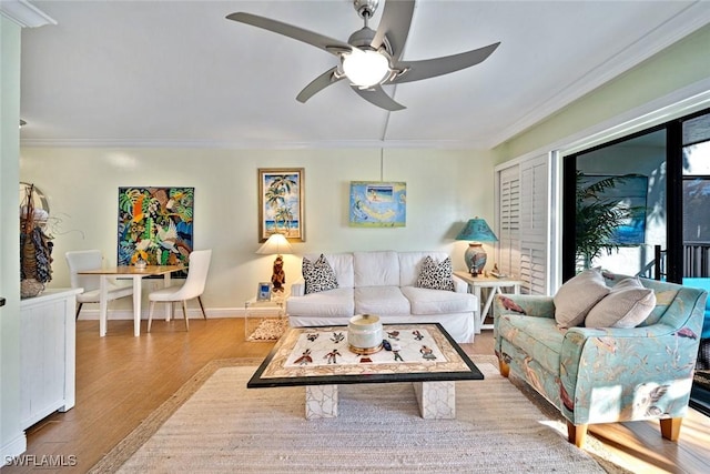 living area with crown molding, wood finished floors, baseboards, and ceiling fan