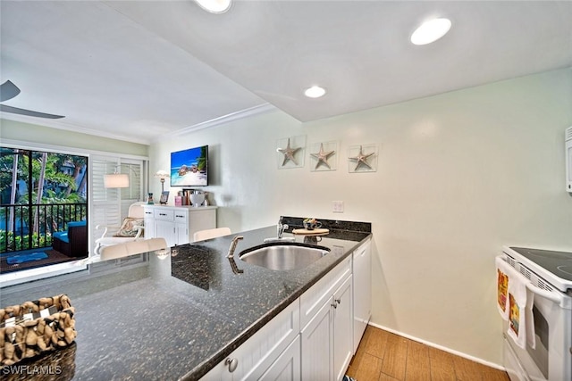 kitchen with white electric stove, dark stone counters, light wood-style flooring, a sink, and white cabinetry