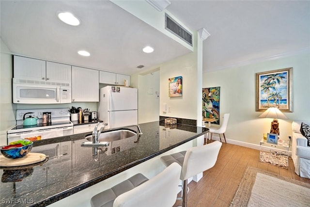 kitchen featuring light wood finished floors, visible vents, dark stone countertops, white appliances, and a sink