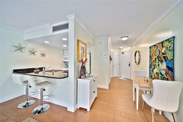 kitchen featuring visible vents, a breakfast bar, ornamental molding, a sink, and light wood-style floors