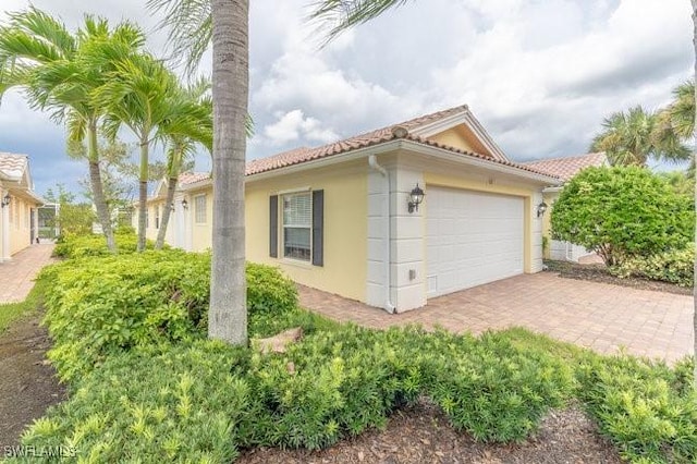 7639 Novara Ct, Naples, FL 34114 - view of side of home featuring decorative driveway, a tile roof, stucco siding, and an attached garage