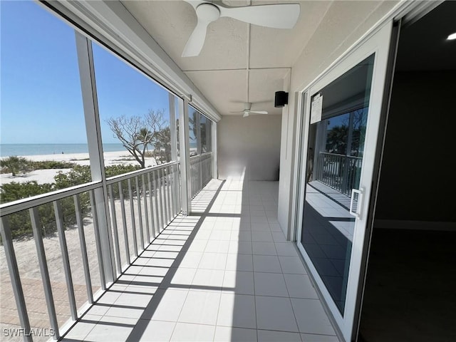 balcony with a view of the beach, a water view, and ceiling fan