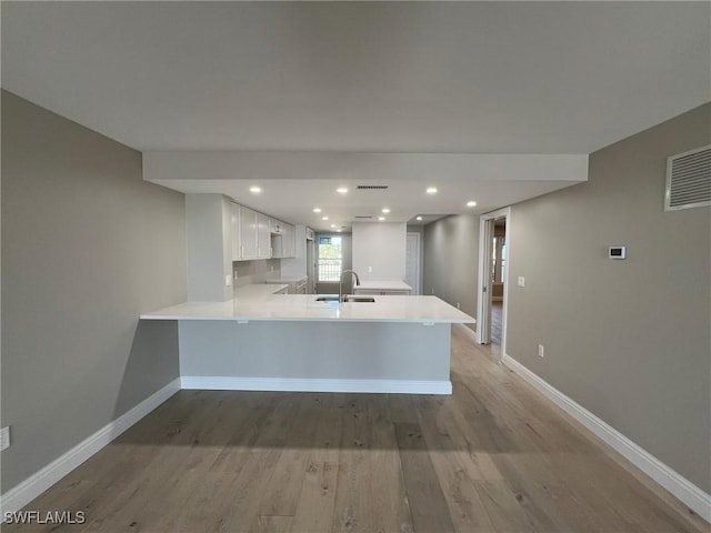 kitchen featuring baseboards, light countertops, a peninsula, white cabinets, and a sink