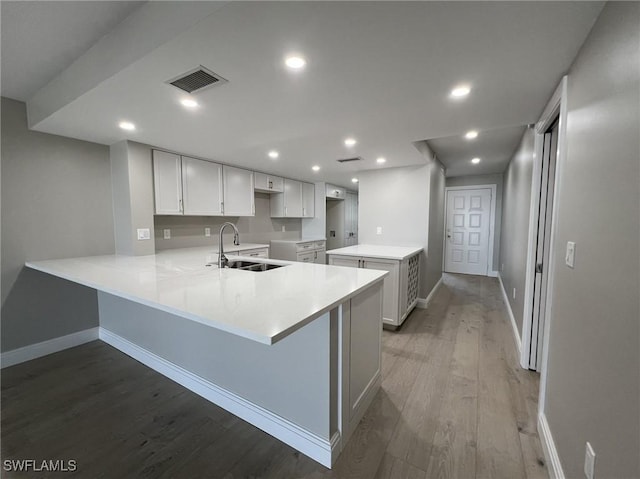 kitchen with visible vents, recessed lighting, a peninsula, wood finished floors, and a sink