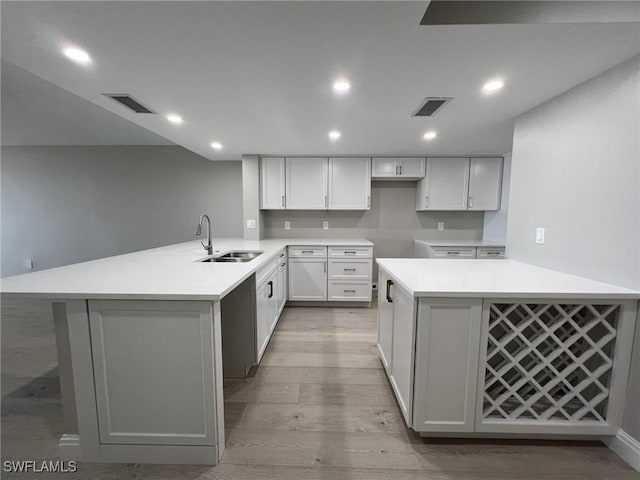 kitchen featuring visible vents, a peninsula, light wood-type flooring, and a sink