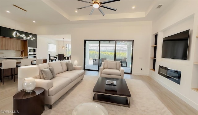 living area featuring visible vents, baseboards, light wood-type flooring, ceiling fan with notable chandelier, and a raised ceiling