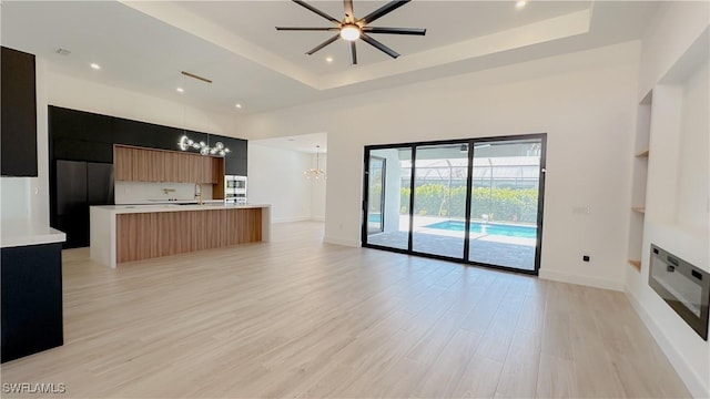 kitchen featuring light wood-type flooring, a tray ceiling, light countertops, modern cabinets, and open floor plan