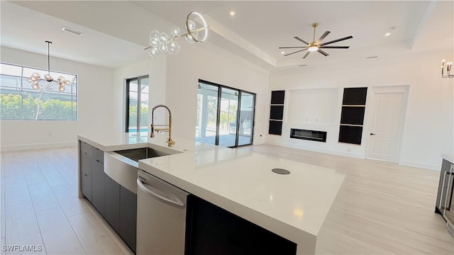 kitchen featuring stainless steel dishwasher, light countertops, open floor plan, and a sink