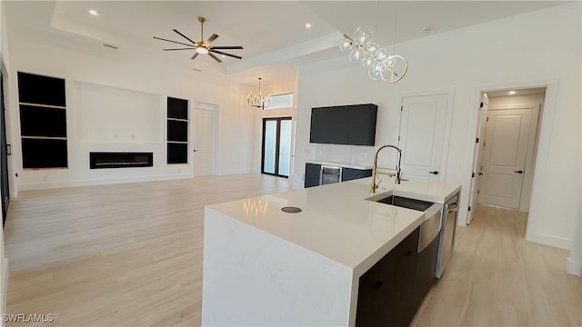 kitchen featuring light wood finished floors, decorative light fixtures, light countertops, a glass covered fireplace, and a kitchen island with sink