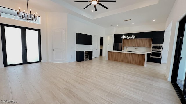 unfurnished living room featuring light wood-type flooring, ceiling fan with notable chandelier, recessed lighting, baseboards, and a towering ceiling