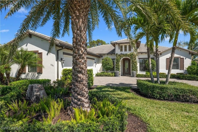 mediterranean / spanish-style home with stucco siding, driveway, a front lawn, and a garage