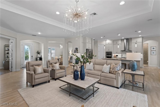 living room featuring arched walkways, light wood-style floors, a tray ceiling, and ornamental molding