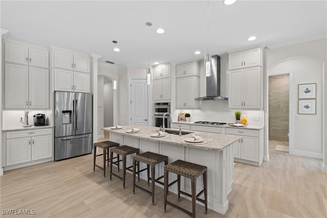 kitchen featuring arched walkways, a sink, decorative backsplash, appliances with stainless steel finishes, and wall chimney range hood