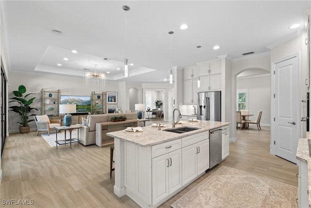 kitchen with a sink, a tray ceiling, white cabinetry, stainless steel appliances, and arched walkways