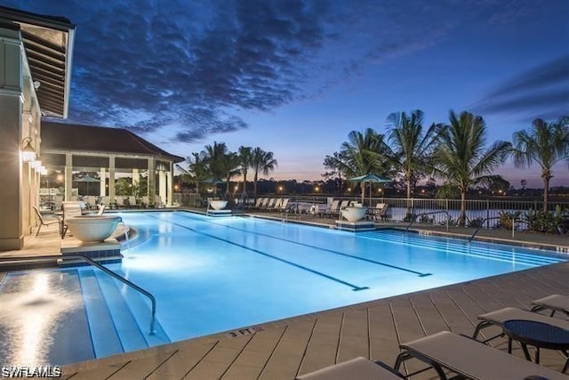 pool at dusk featuring a community pool and fence