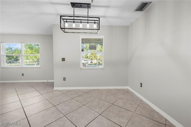 empty room featuring light tile patterned floors, visible vents, baseboards, and a textured ceiling