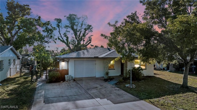 ranch-style home featuring stucco siding, driveway, a gate, a front yard, and an attached garage