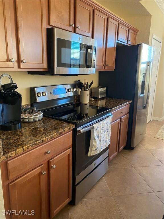 kitchen with dark stone counters, light tile patterned flooring, brown cabinetry, and stainless steel appliances