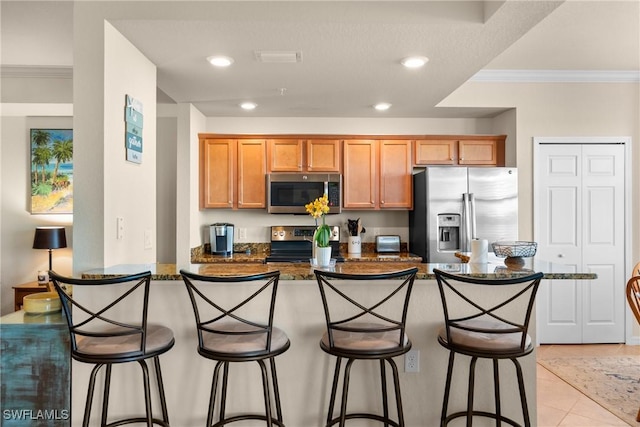 kitchen with a kitchen breakfast bar, appliances with stainless steel finishes, dark stone countertops, ornamental molding, and recessed lighting