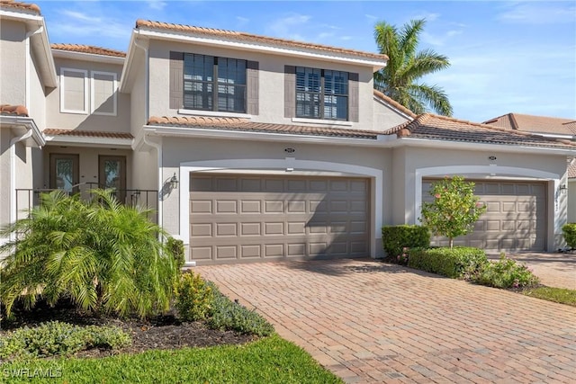 view of front facade featuring stucco siding, an attached garage, a tile roof, and decorative driveway