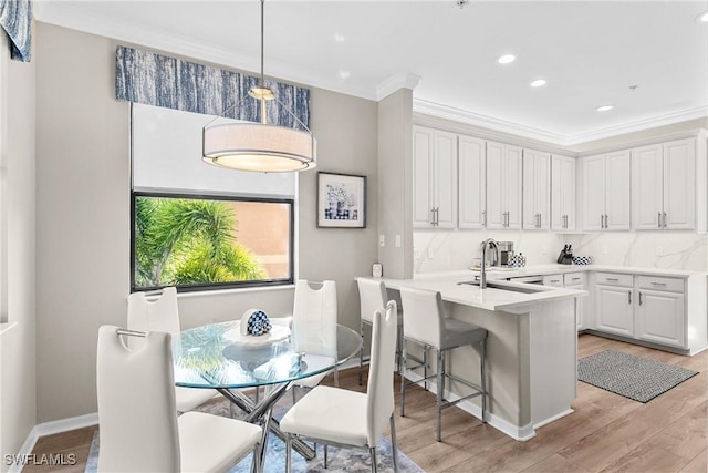 kitchen featuring white cabinets, ornamental molding, light wood-type flooring, and a sink