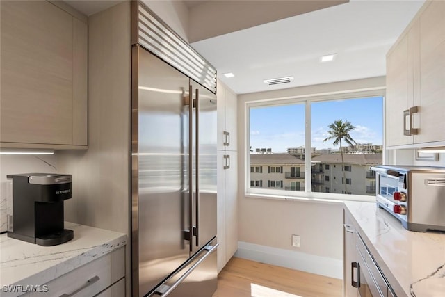 kitchen with light stone countertops, visible vents, light wood finished floors, a toaster, and stainless steel built in refrigerator