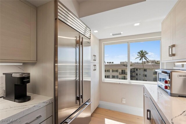 kitchen with visible vents, light wood-style flooring, built in fridge, a toaster, and light stone countertops