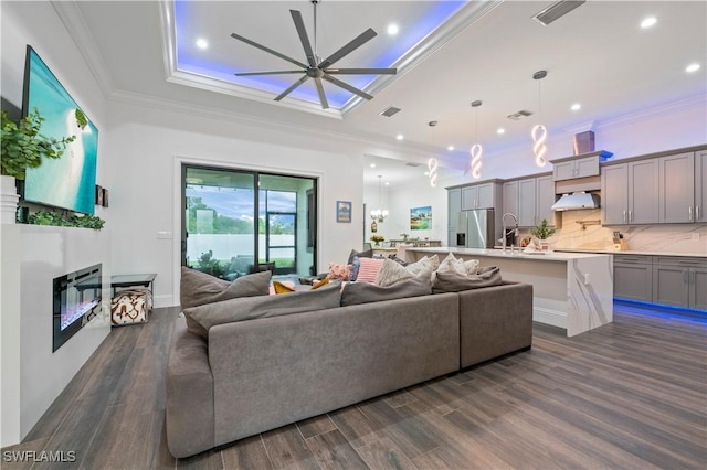 living room with a glass covered fireplace, dark wood-type flooring, ornamental molding, and ceiling fan