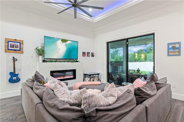 living room with ceiling fan, a glass covered fireplace, dark wood finished floors, and ornamental molding