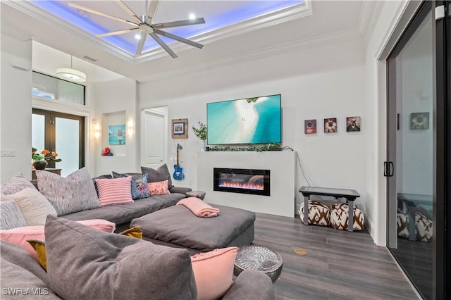 living room with visible vents, a tray ceiling, dark wood-style flooring, ornamental molding, and a glass covered fireplace