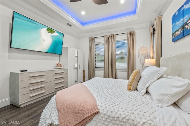 bedroom with visible vents, dark wood-type flooring, ornamental molding, a ceiling fan, and a raised ceiling