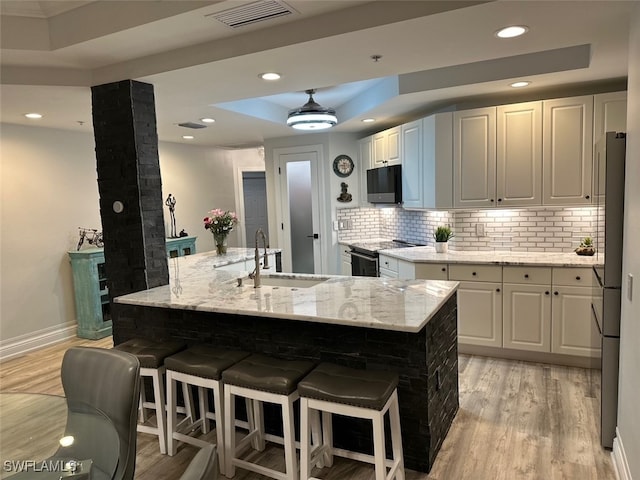 kitchen featuring visible vents, light wood-type flooring, a tray ceiling, stainless steel appliances, and a sink