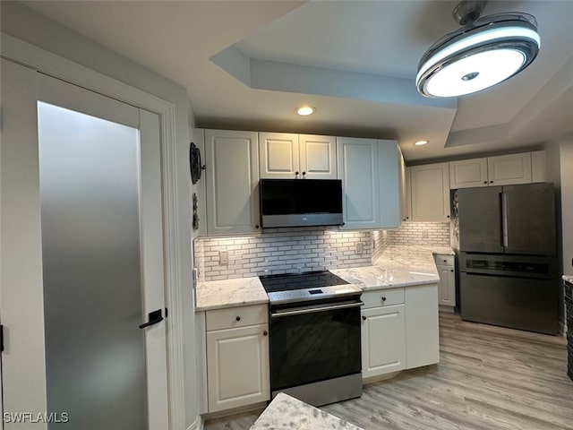 kitchen with a tray ceiling, tasteful backsplash, light wood-style floors, and appliances with stainless steel finishes