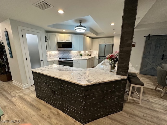 kitchen featuring a tray ceiling, light stone counters, decorative backsplash, appliances with stainless steel finishes, and light wood-style floors