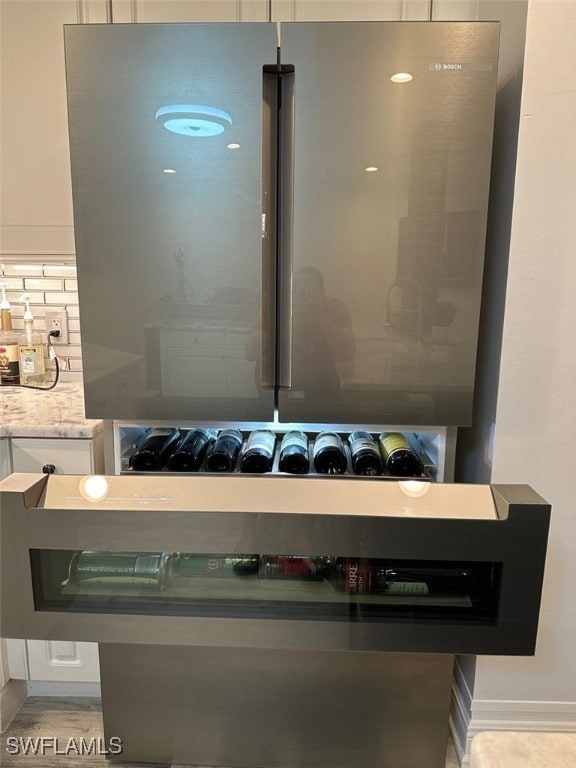 interior details featuring white cabinetry, decorative backsplash, light stone counters, and freestanding refrigerator