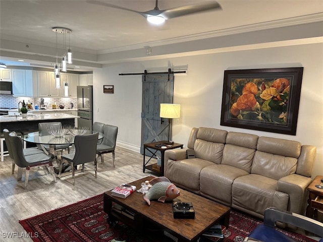 living room featuring light wood-style floors, baseboards, crown molding, and a barn door