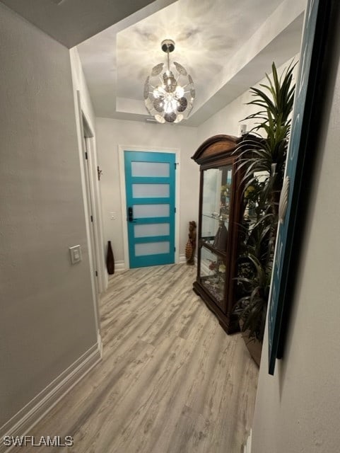 entryway featuring an inviting chandelier, a raised ceiling, baseboards, and light wood-type flooring