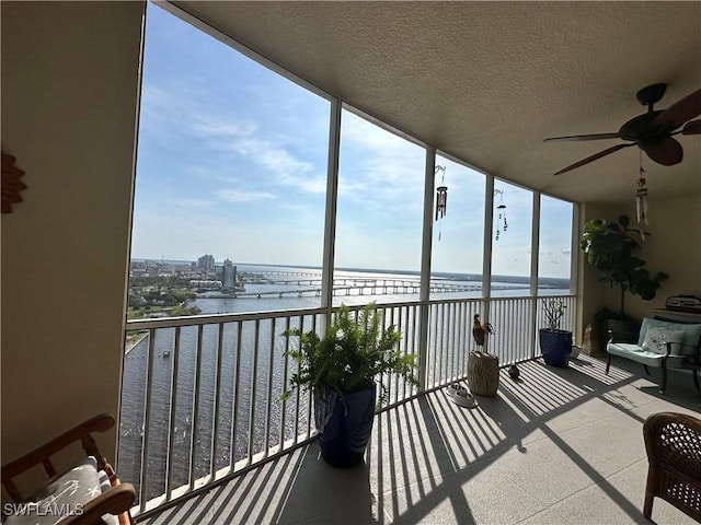 sunroom with ceiling fan and a water view