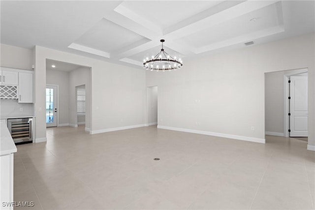 interior space featuring beverage cooler, coffered ceiling, a bar, baseboards, and a chandelier