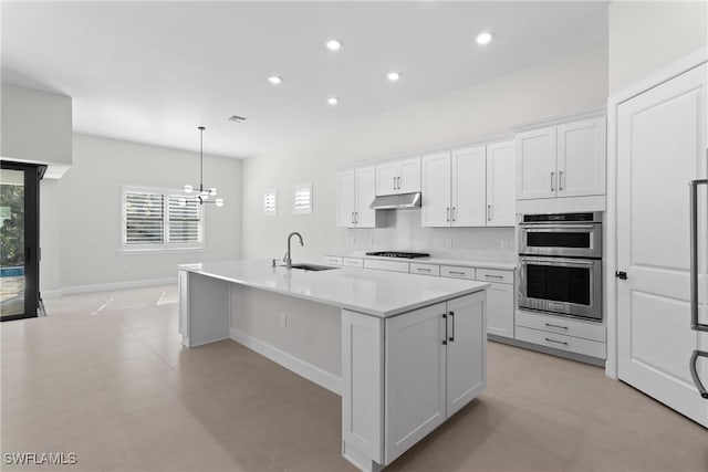 kitchen with an island with sink, a sink, under cabinet range hood, gas cooktop, and light countertops