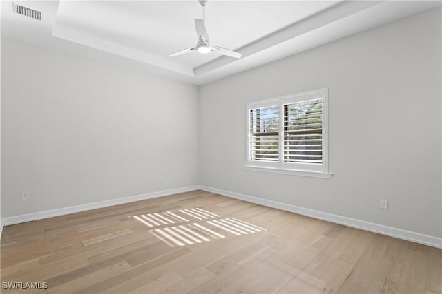 unfurnished room featuring visible vents, baseboards, a tray ceiling, and wood finished floors