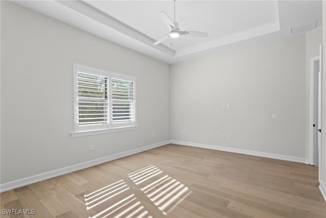 empty room with baseboards, light wood-style floors, a tray ceiling, and a ceiling fan