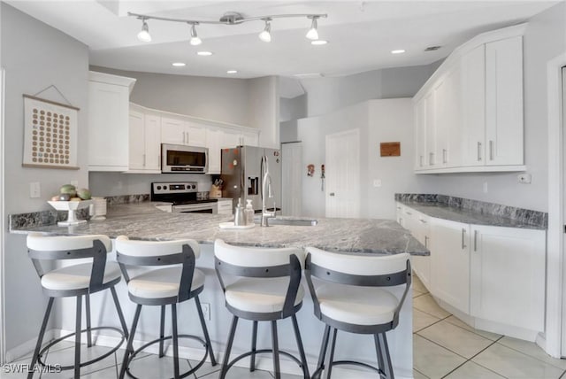 kitchen featuring light tile patterned floors, appliances with stainless steel finishes, a peninsula, white cabinets, and a sink