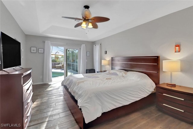 bedroom featuring a raised ceiling, access to outside, hardwood / wood-style floors, baseboards, and ceiling fan