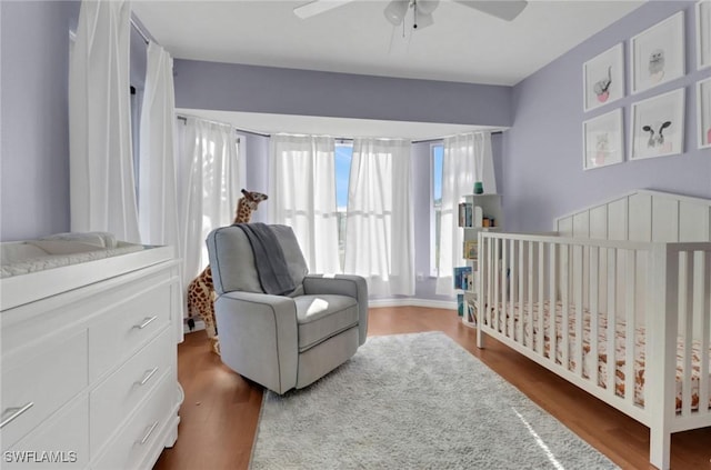 bedroom featuring a crib, ceiling fan, and wood finished floors