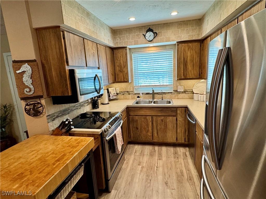 kitchen with light wood-style flooring, a sink, a textured ceiling, appliances with stainless steel finishes, and brown cabinetry